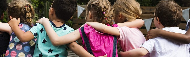 Eine Reihe Kinder sitzen Arm un Arm auf einer Mauer